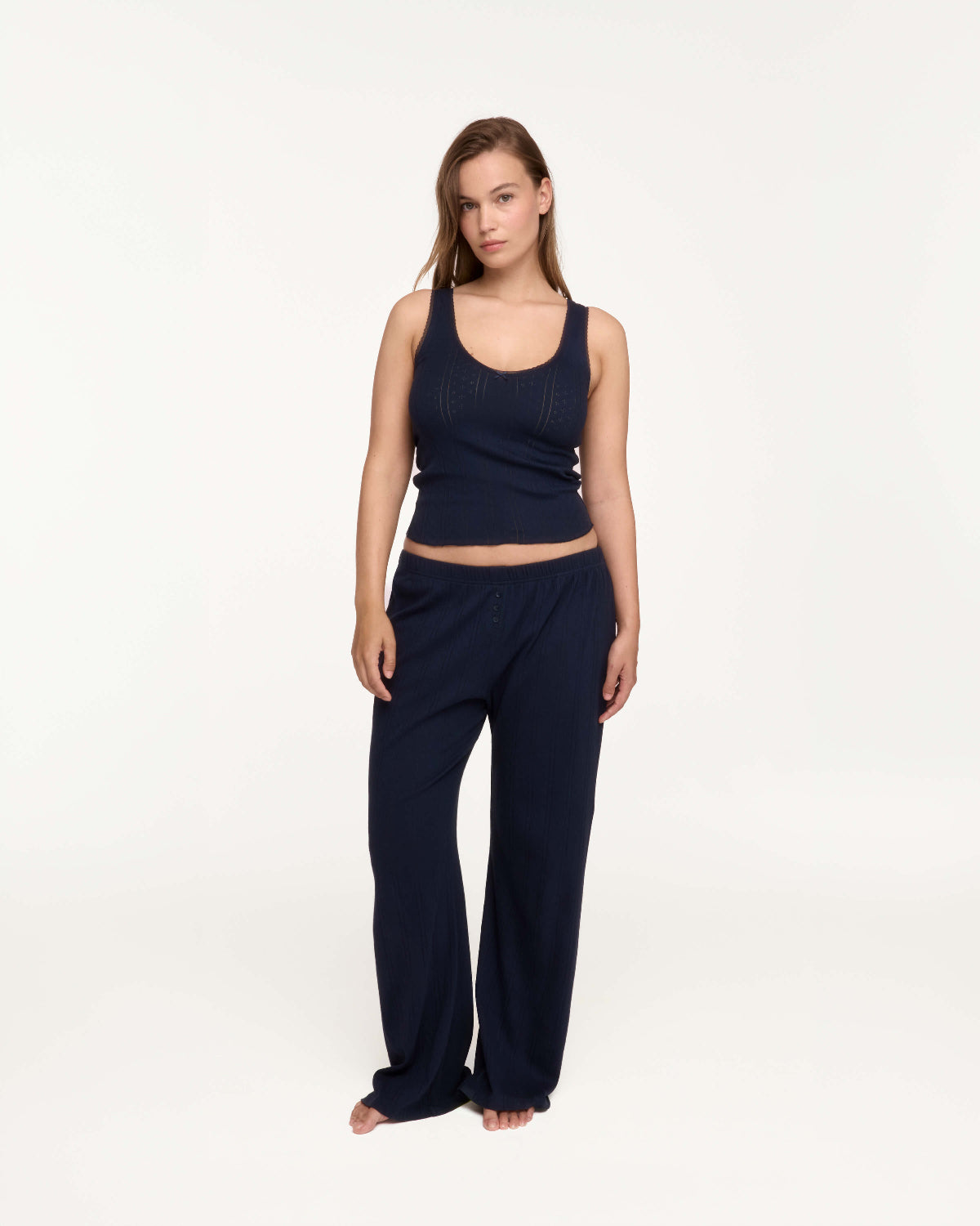 A woman modeling a matching navy blue lounge set consisting of a ribbed tank top and wide-leg pants, standing against a plain white studio background.