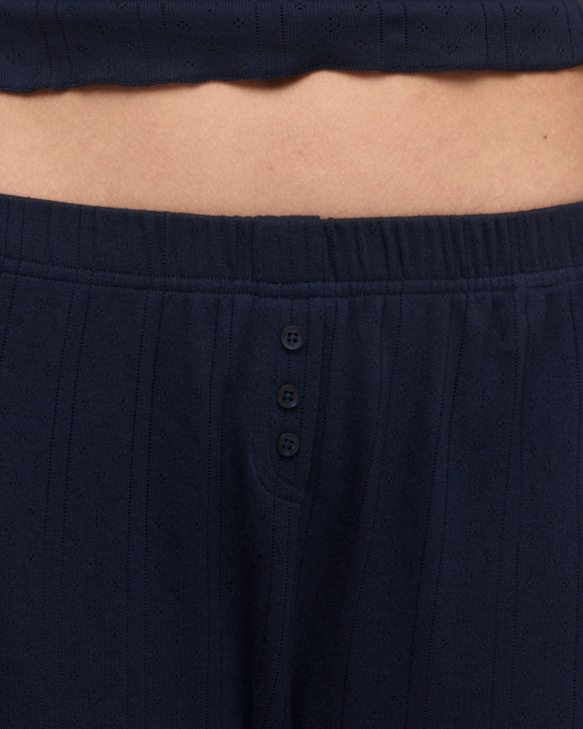 Close-up of a person wearing dark navy pants with a three-button placket and a matching cropped top.