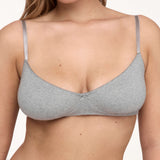 A woman wearing a light gray bra with thin shoulder straps, shown from the chest up against a plain light background.