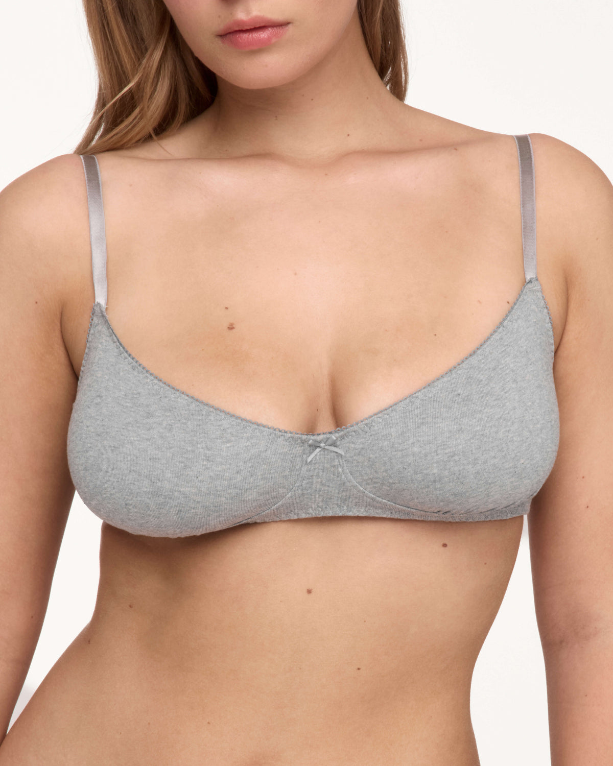 A woman wearing a light gray bra with thin shoulder straps, shown from the chest up against a plain light background.