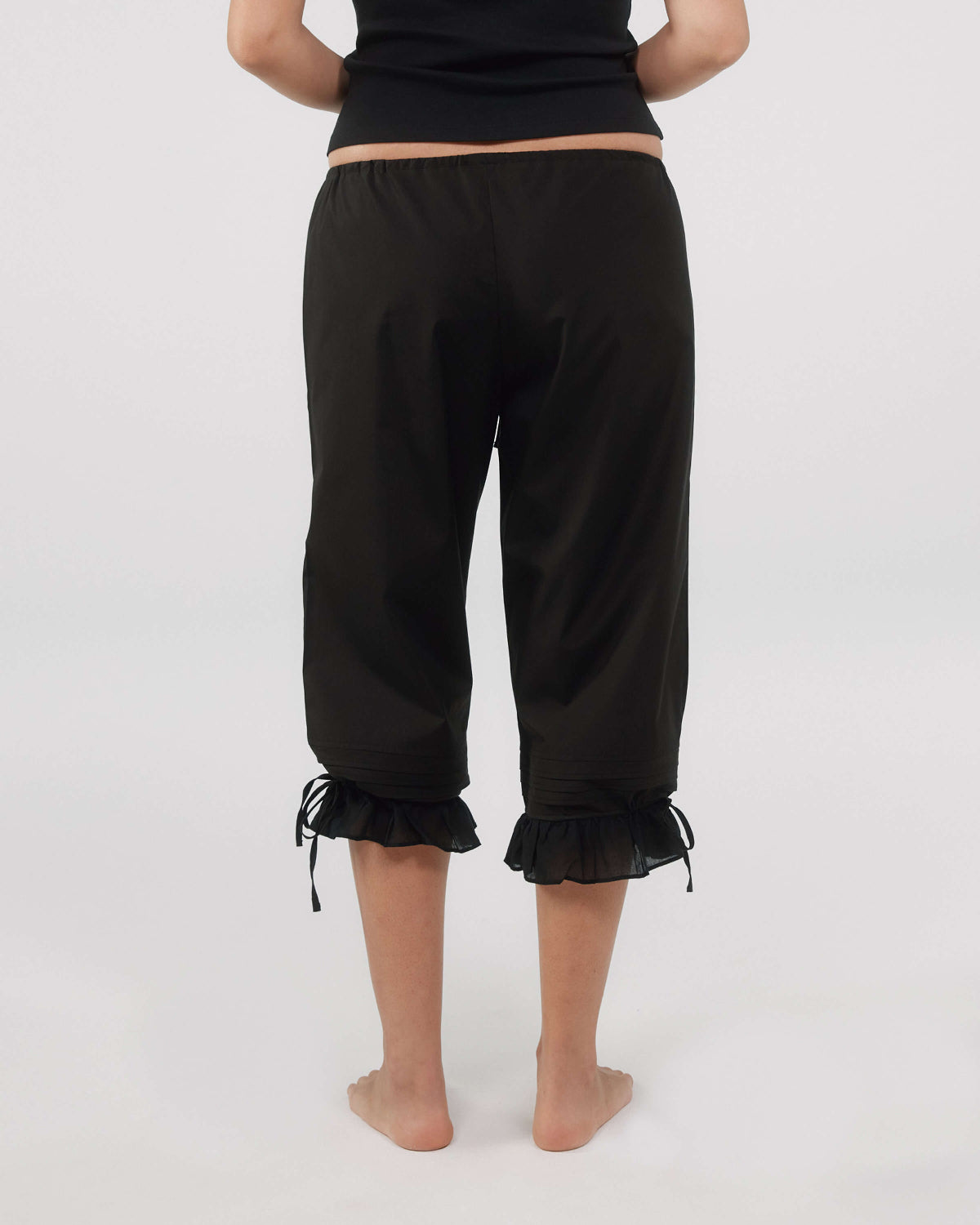 Person wearing black capri pants with ruffled cuffs on a white background