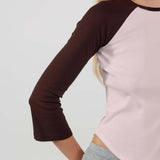 Person wearing a pink and brown long-sleeve shirt with gray pants on a white background