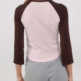 Person wearing a pink and brown long-sleeve top with gray shorts on a plain background