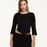 A model wearing a black three-quarter sleeve top and matching black ribbed mini skirt against a plain white studio background.