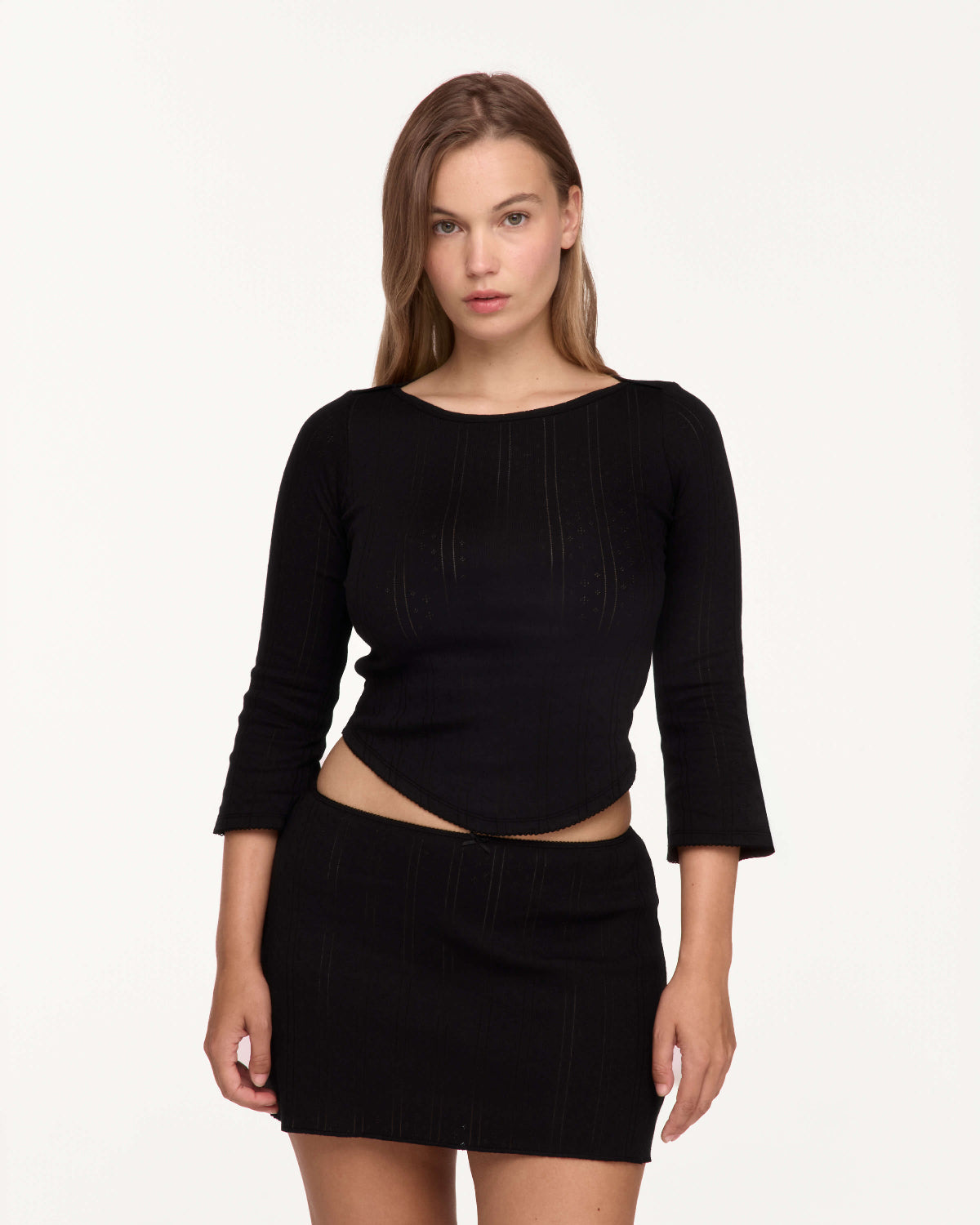 A model wearing a black three-quarter sleeve top and matching black ribbed mini skirt against a plain white studio background.