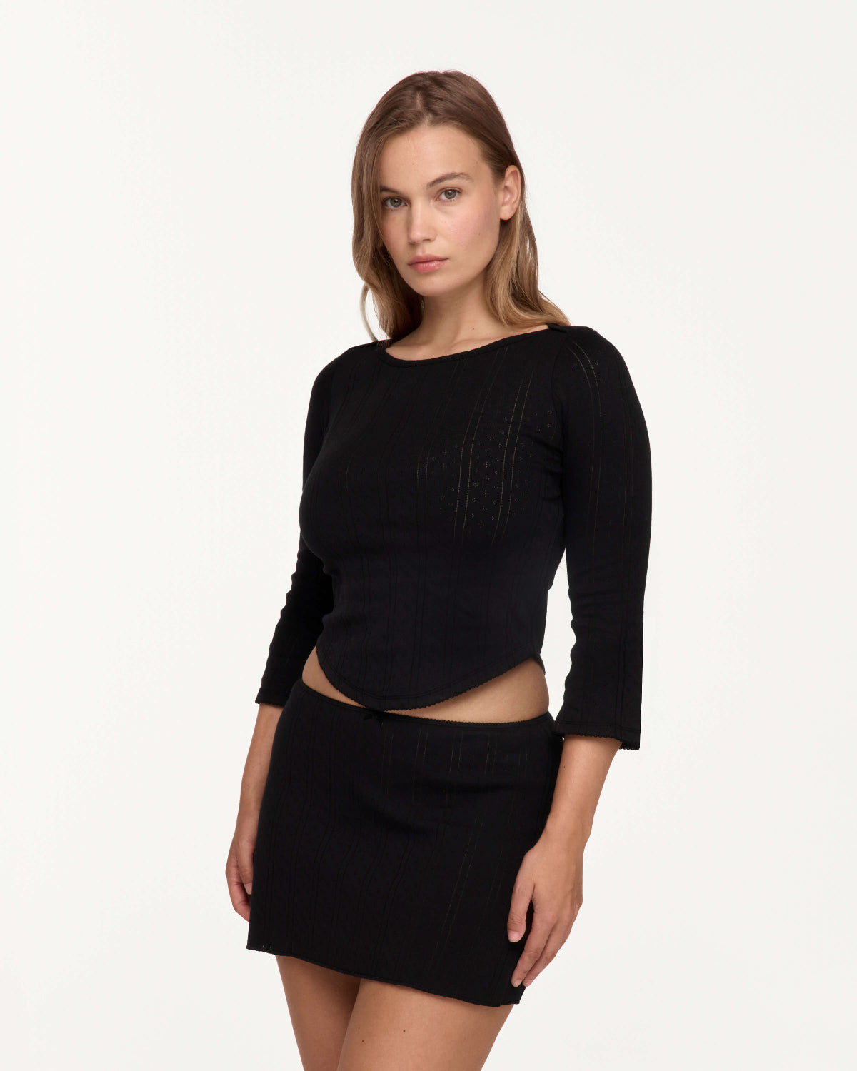 A woman modeling a black three-quarter sleeve top and matching mini skirt set against a plain white studio background.
