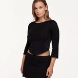 A woman modeling a black three-quarter sleeve top and matching mini skirt set against a plain white studio background.