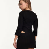 A woman shown from the back wearing a black long-sleeve top and a matching black mini skirt, against a plain white studio background.