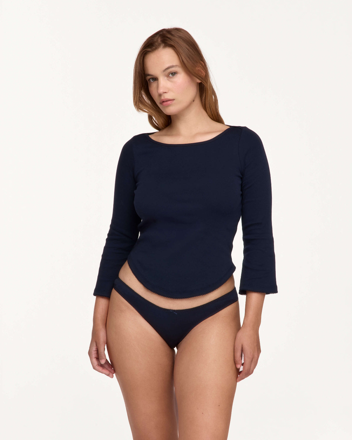 A woman modeling a navy blue three-quarter sleeve top and matching navy blue bikini bottoms against a plain white studio background.