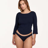 A woman modeling a navy blue three-quarter sleeve top and matching navy blue bikini bottoms against a plain white studio background.