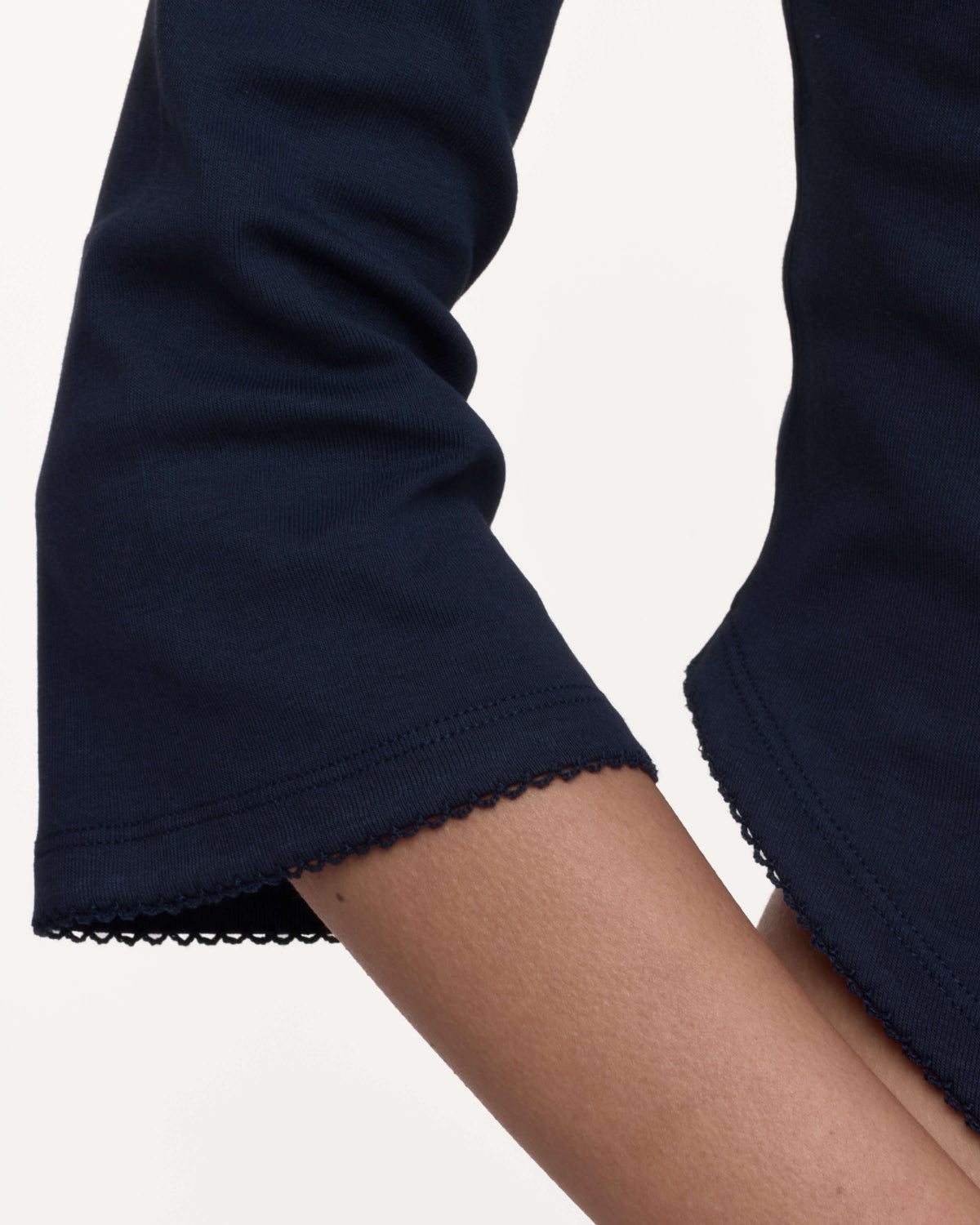 Close-up of a navy blue sleeve with a scalloped hem, worn on a model's arm against a plain light background.