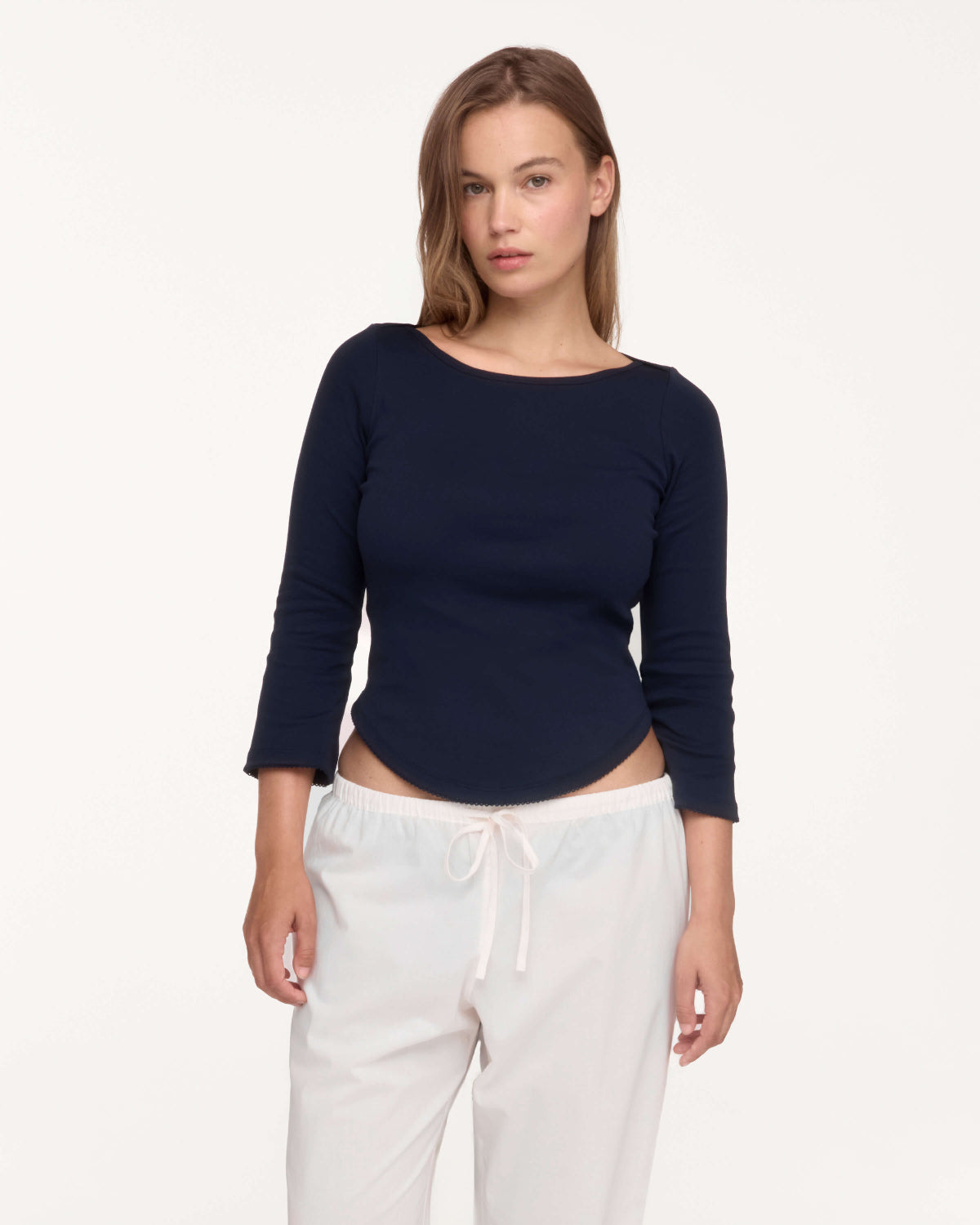 A woman modeling a navy blue long-sleeve boat-neck top, paired with white drawstring sweatpants, against a plain white studio background.