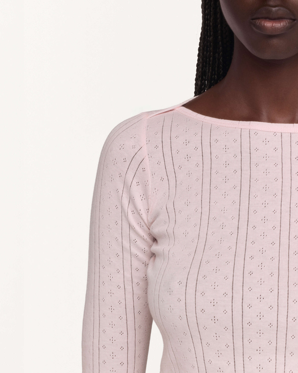 Close-up of a model wearing a light pink long-sleeve top with a boat neckline against a plain off-white background.