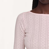 Close-up of a model wearing a light pink long-sleeve top with a boat neckline against a plain off-white background.