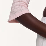 Close-up of a model wearing a light pink top with a scalloped hem against a plain off-white background.