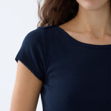 Close-up of a woman wearing a dark navy blue short-sleeve top with a boat neckline and delicate scalloped lace trim on the sleeve.