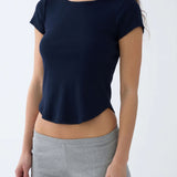 A woman wearing a navy blue short-sleeve top and light gray heather shorts, shown from the neck down against a plain light gray studio background.