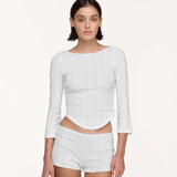 A model wearing a white three-quarter sleeve top and matching white shorts against a plain off-white studio background.