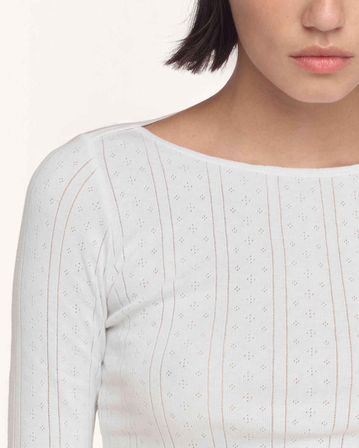 Close-up of a model wearing a white long-sleeve top with a boat neckline against a plain light background.