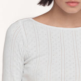 Close-up of a model wearing a white long-sleeve top with a boat neckline against a plain light background.