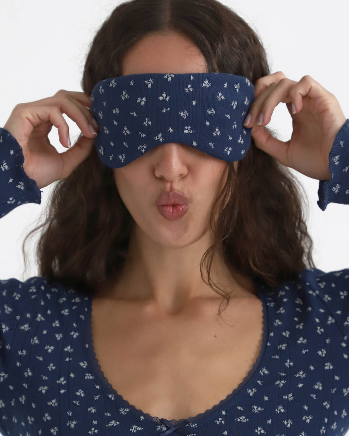 Woman wearing a blue sleep mask with white patterns, posing playfully.