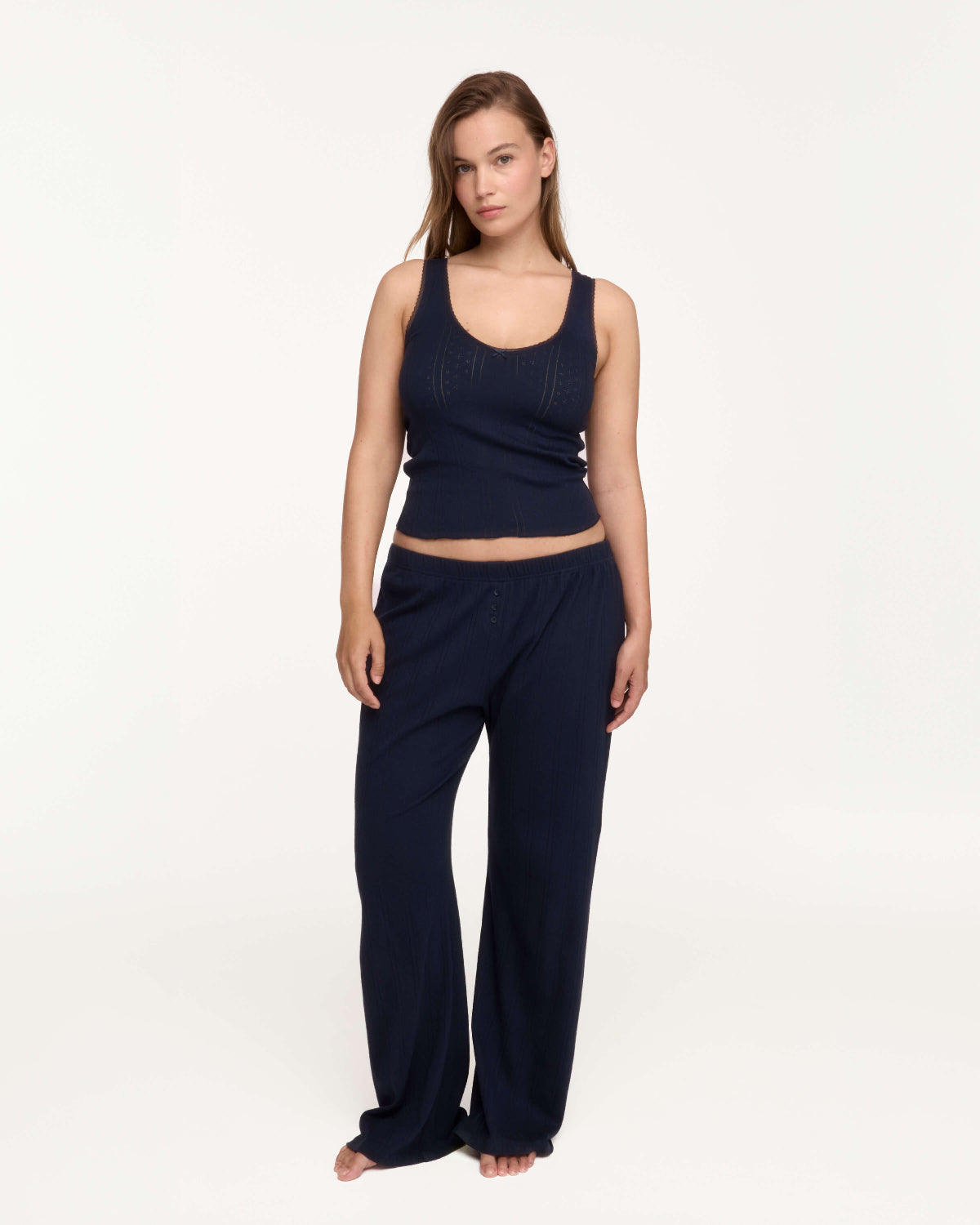 A woman in a matching navy blue loungewear set consisting of a sleeveless cropped tank top and wide-leg pants, photographed against a clean white studio background.