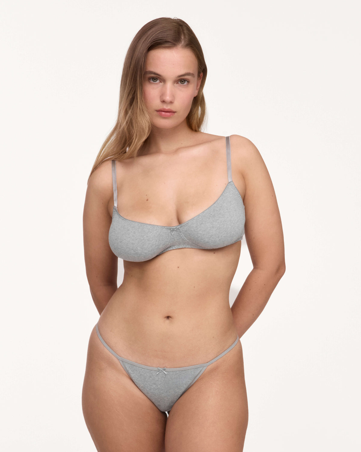 A woman modeling a light gray set against a plain off-white studio background.