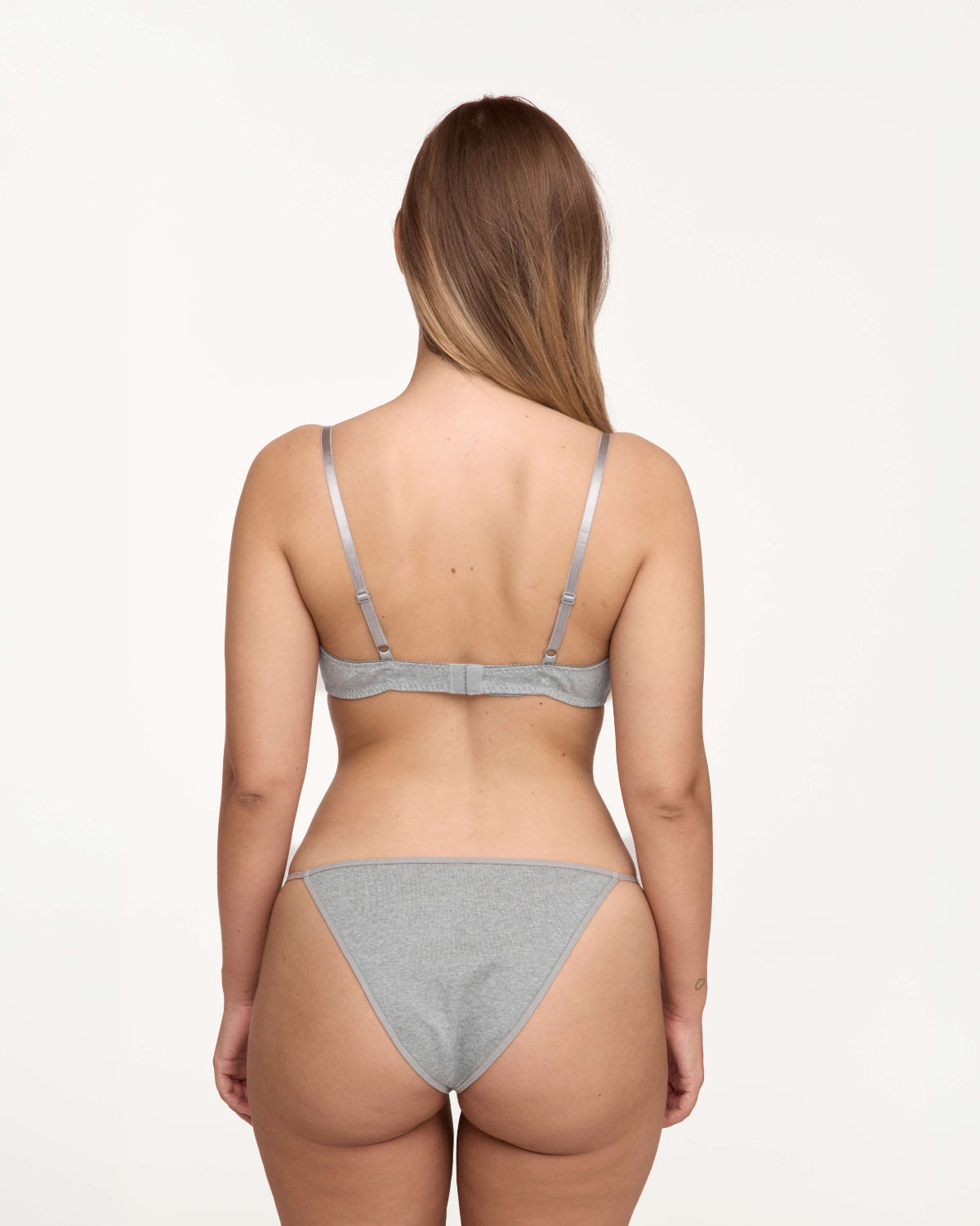 A woman shown from the back wearing a light gray set against a plain white studio background.