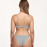 A woman shown from the back wearing a light gray set against a plain white studio background.