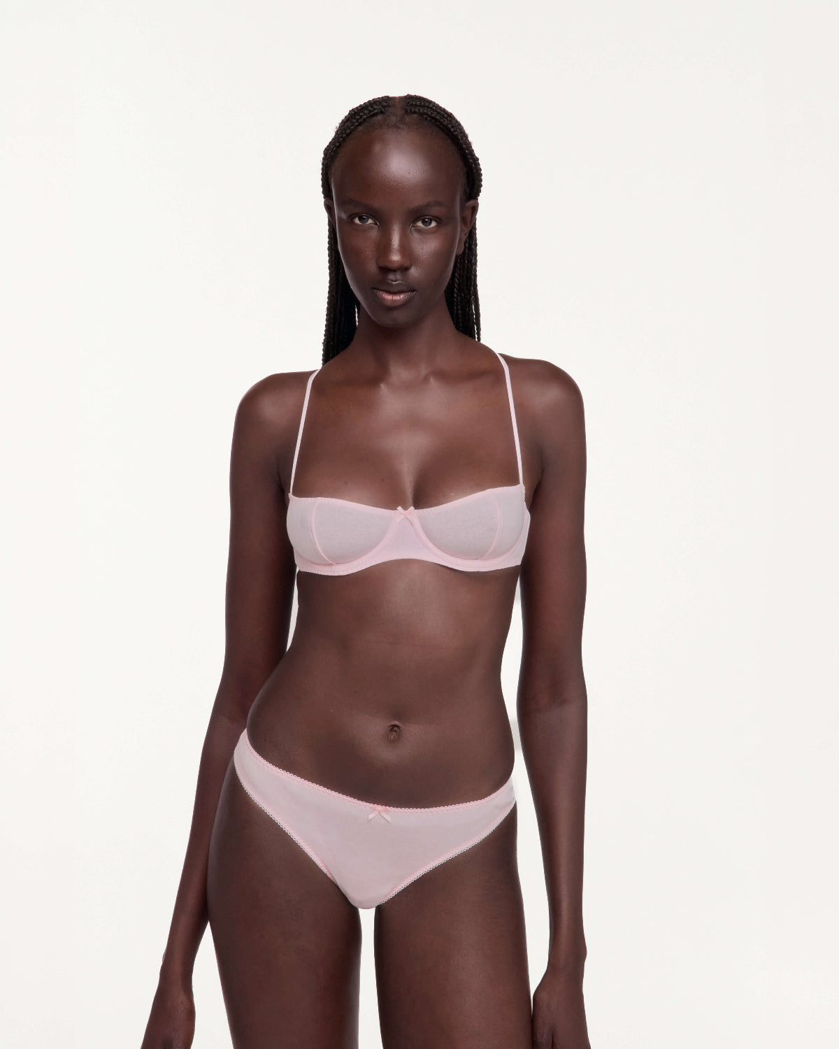 A model wearing a light pink bra and matching underwear set, photographed against a solid off-white studio background.