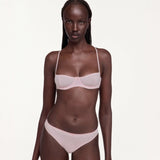 A model wearing a light pink bra and matching underwear set, photographed against a solid off-white studio background.