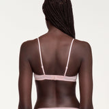 A woman viewed from the back wearing a pale pink bralette with thin adjustable straps and a matching light pink bottom, against a plain light background.