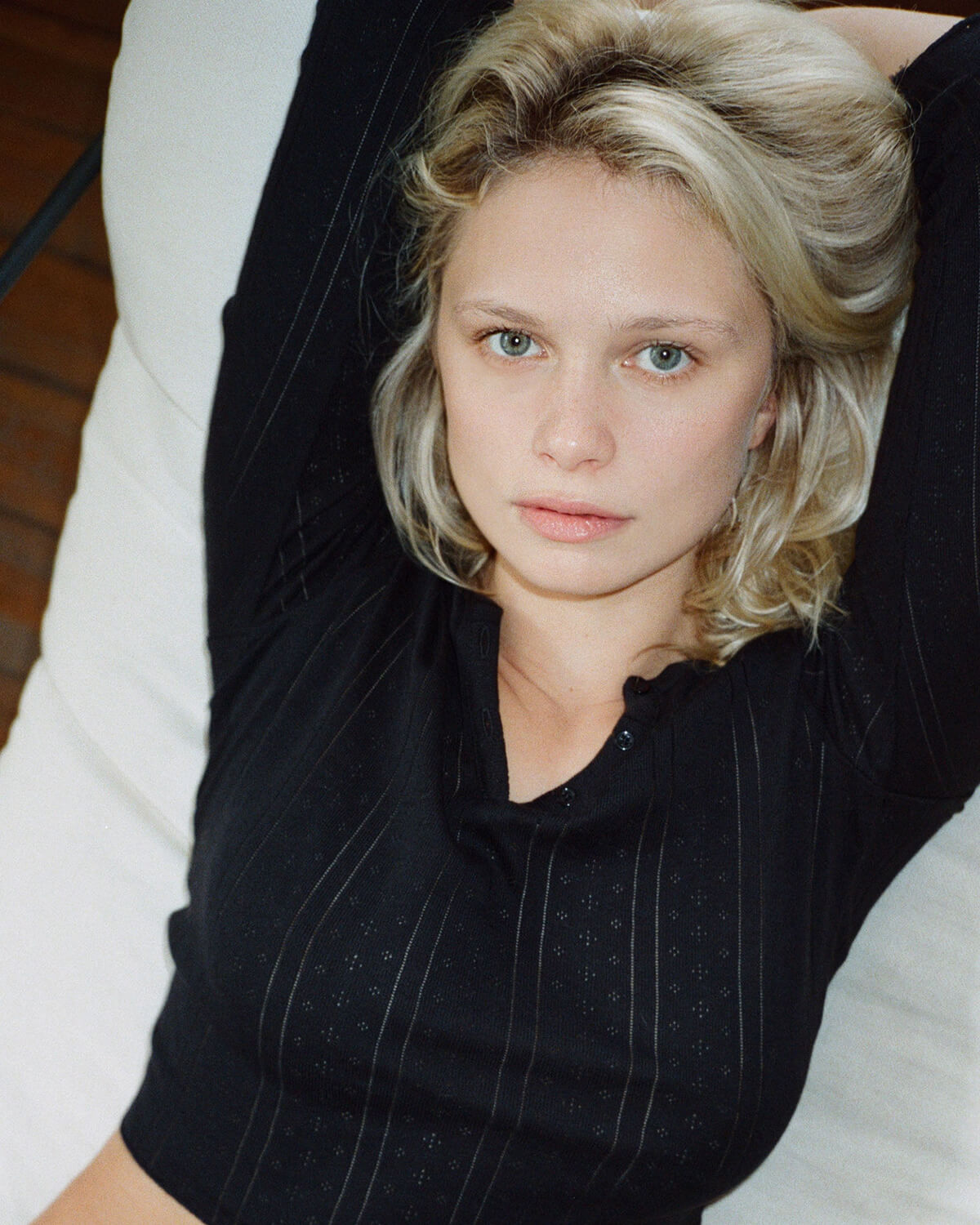 Woman with blonde hair wearing a black pinstripe shirt sitting on a white couch.