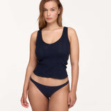 A woman modeling a dark navy blue ribbed knit two-piece set consisting of a scoop-neck tank top and matching low-rise briefs, shot against a solid off-white studio background.