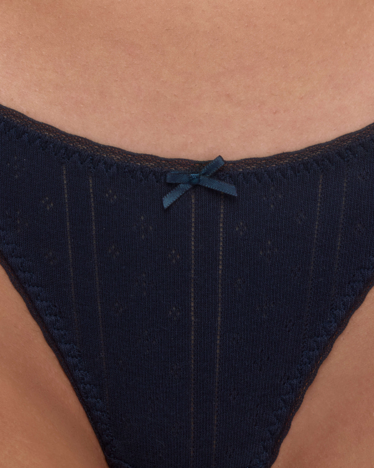 Close-up of a person wearing a dark navy blue lace thong with a small matching bow at the center front.