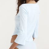 Woman wearing a light blue long-sleeve top and white shorts on a plain background