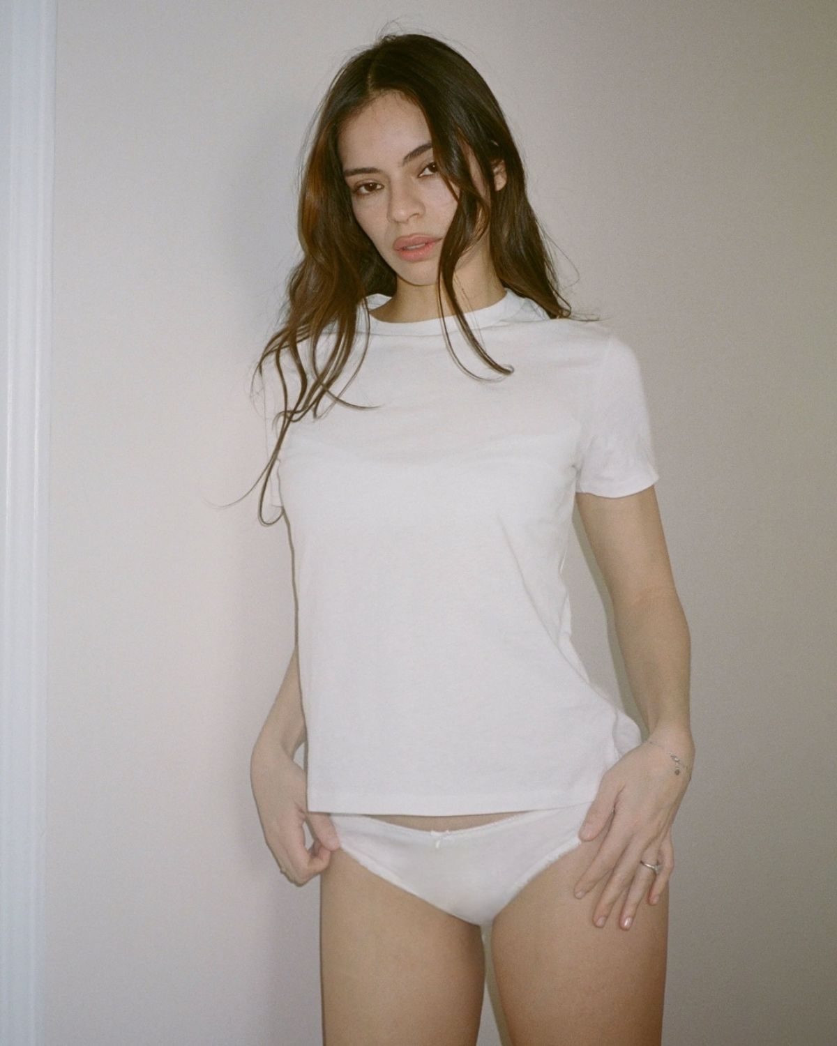 Woman wearing a plain white t-shirt and underwear against a neutral background