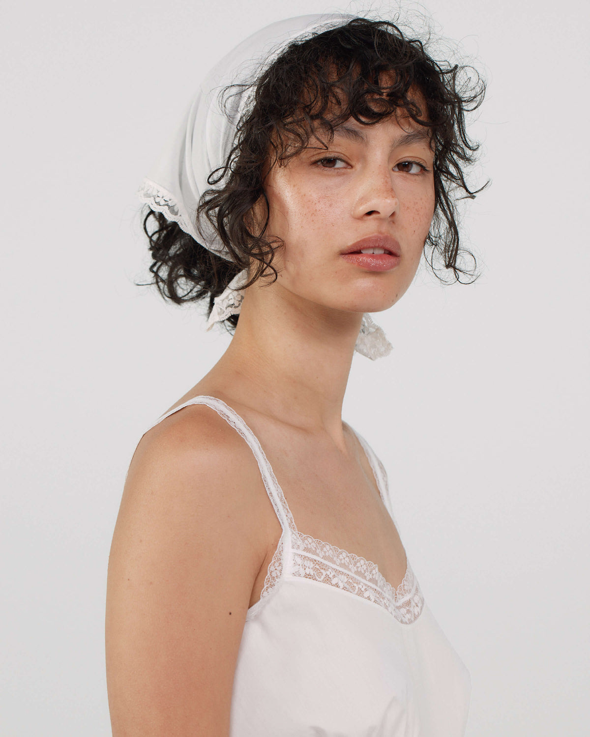 Woman wearing a white lace headscarf and a white dress against a plain background