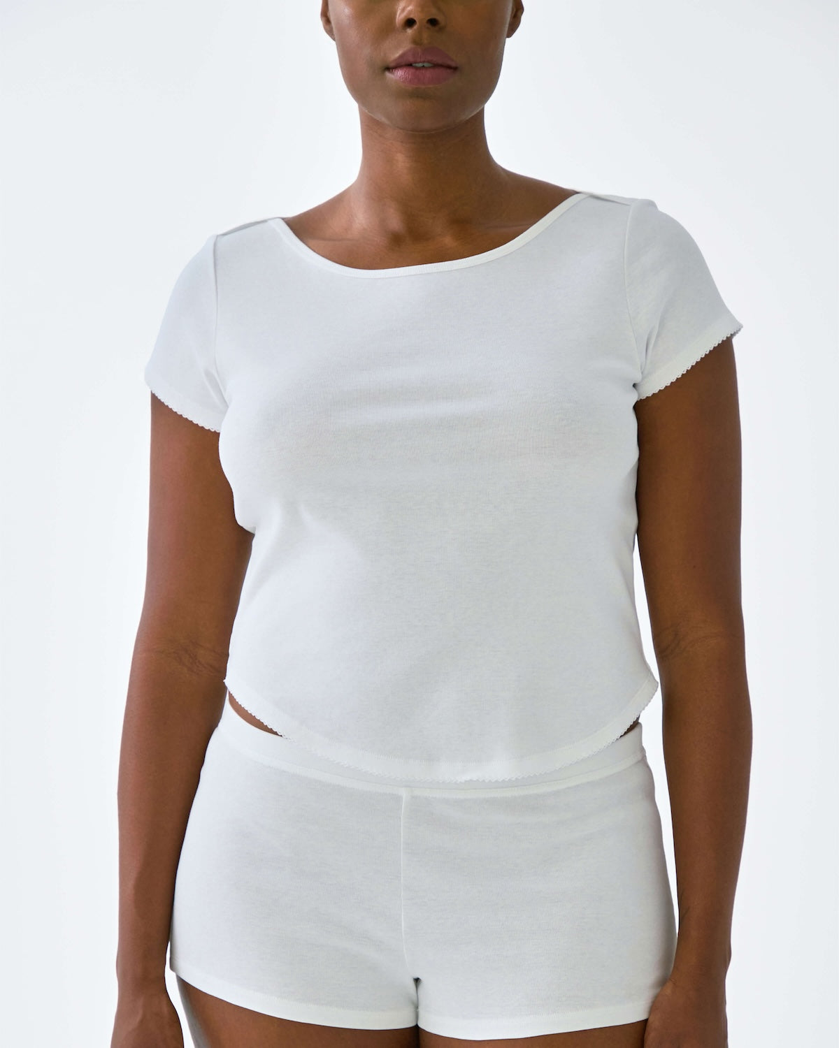 Person wearing a white top and shorts set on a plain background