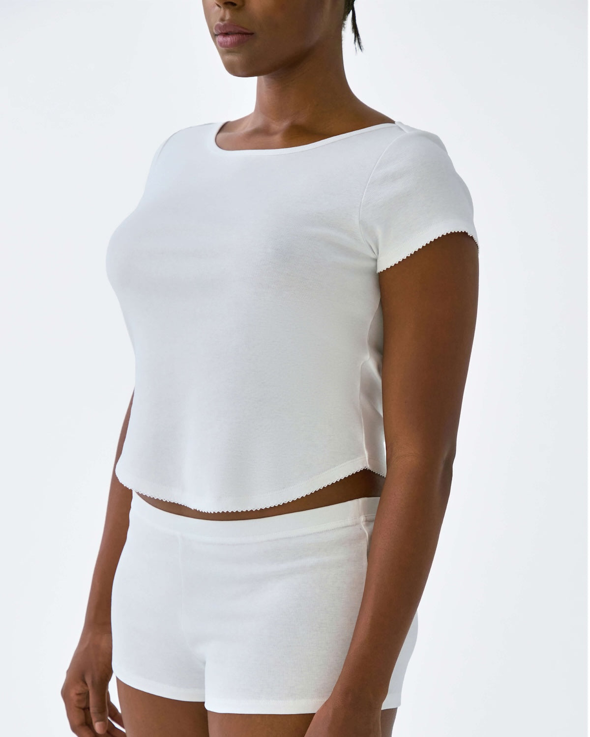 Person wearing a white crop top and shorts on a plain background
