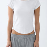 A woman wearing a white short-sleeve crop top with scalloped edges and gray heathered lounge pants, shown from the neck down against a plain white background.