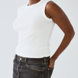 Person wearing a white sleeveless top and dark jeans on a plain background